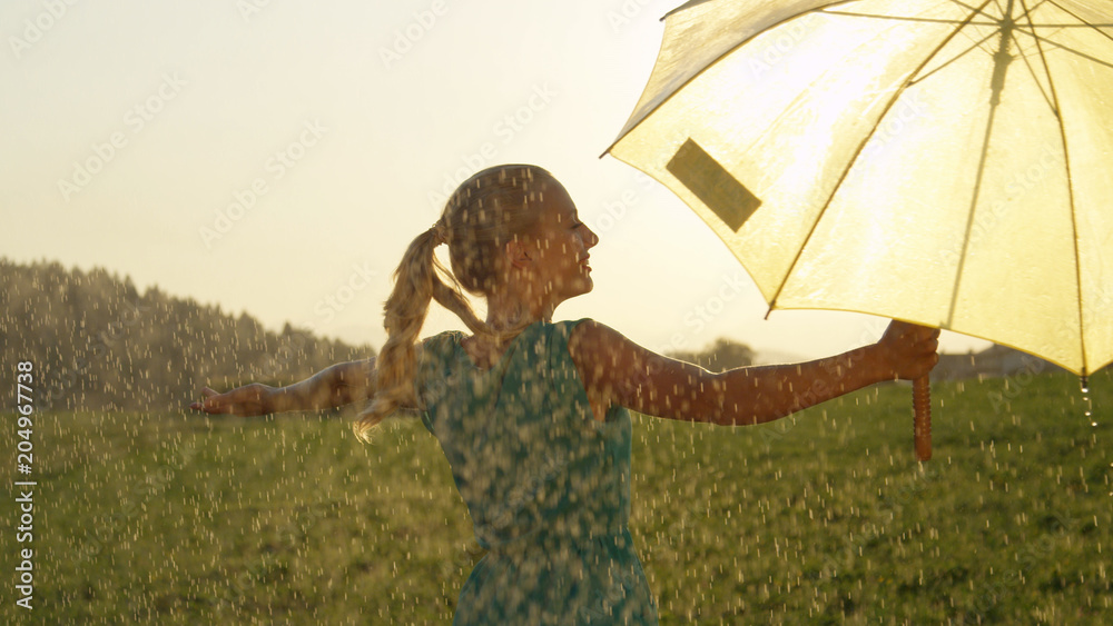 特写：壮观的金色阳光照射在雨中跳舞的无忧无虑的女人身上。