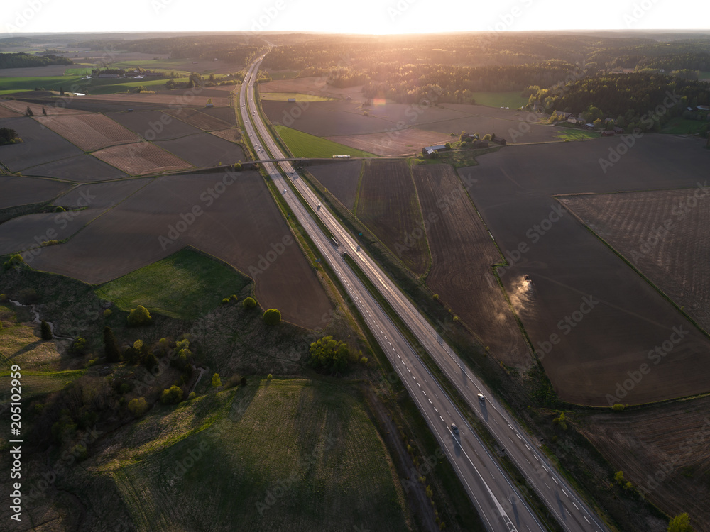 通往落日的公路鸟瞰图，公路上有汽车，田野上有拖拉机