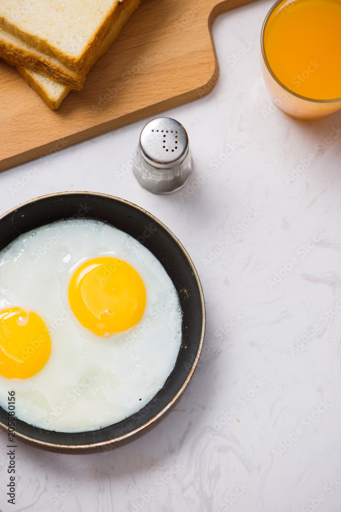 Eating in the process, fried eggs in a frying pan, toast  and orange juice for breakfast on a white 