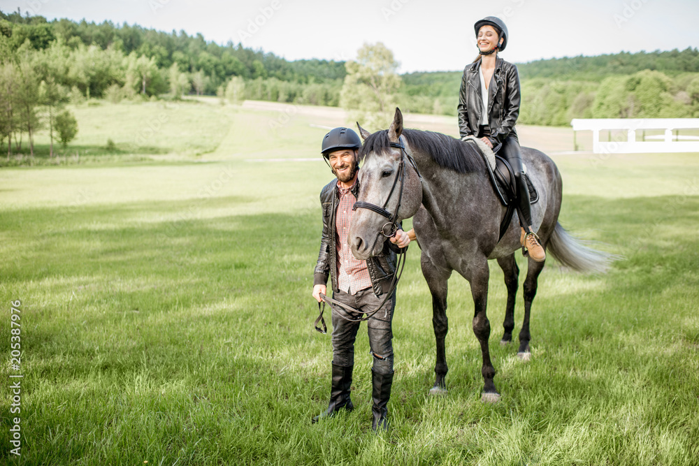 Man leading a horse with woman rider on the beautiful green meadow during the sunny weather