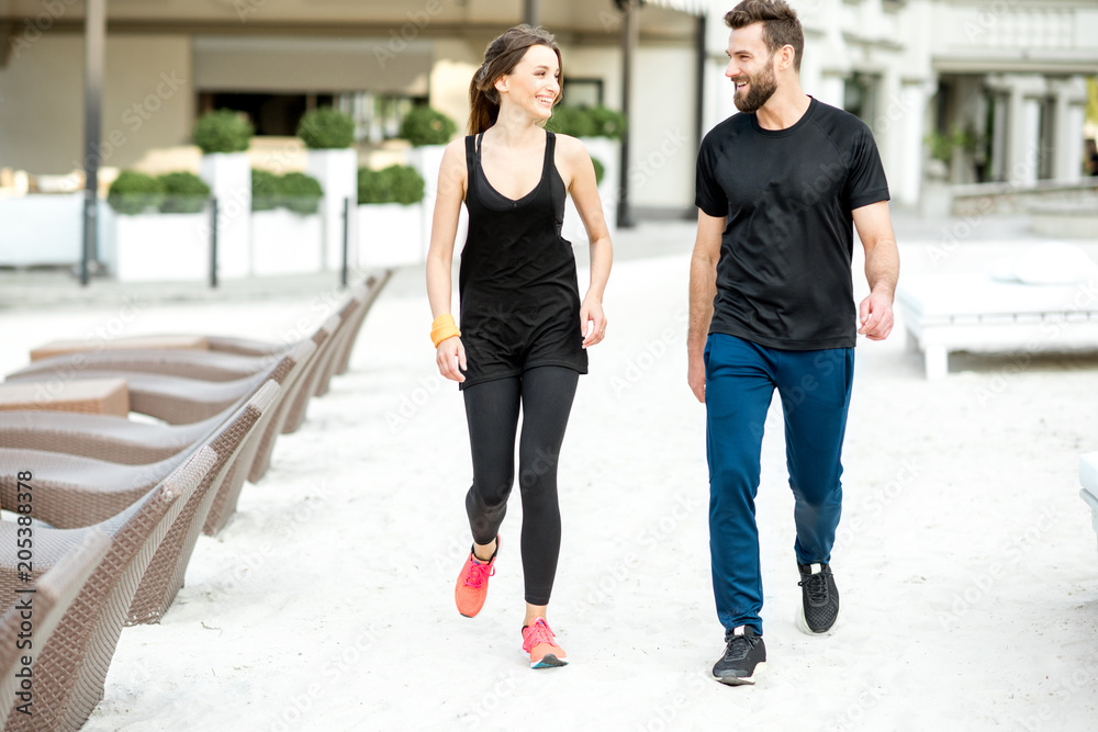 Couple in black sportswear walking on the beach in the resort