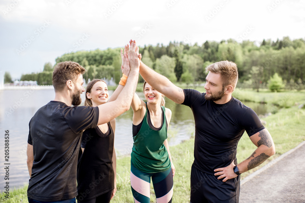 Sports team having fun putting hands together after the training outdoors in the park near the lake