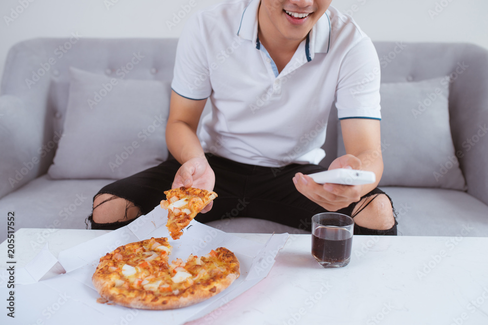 男人看电视，用软饮料吃披萨。特写。坐在沙发上