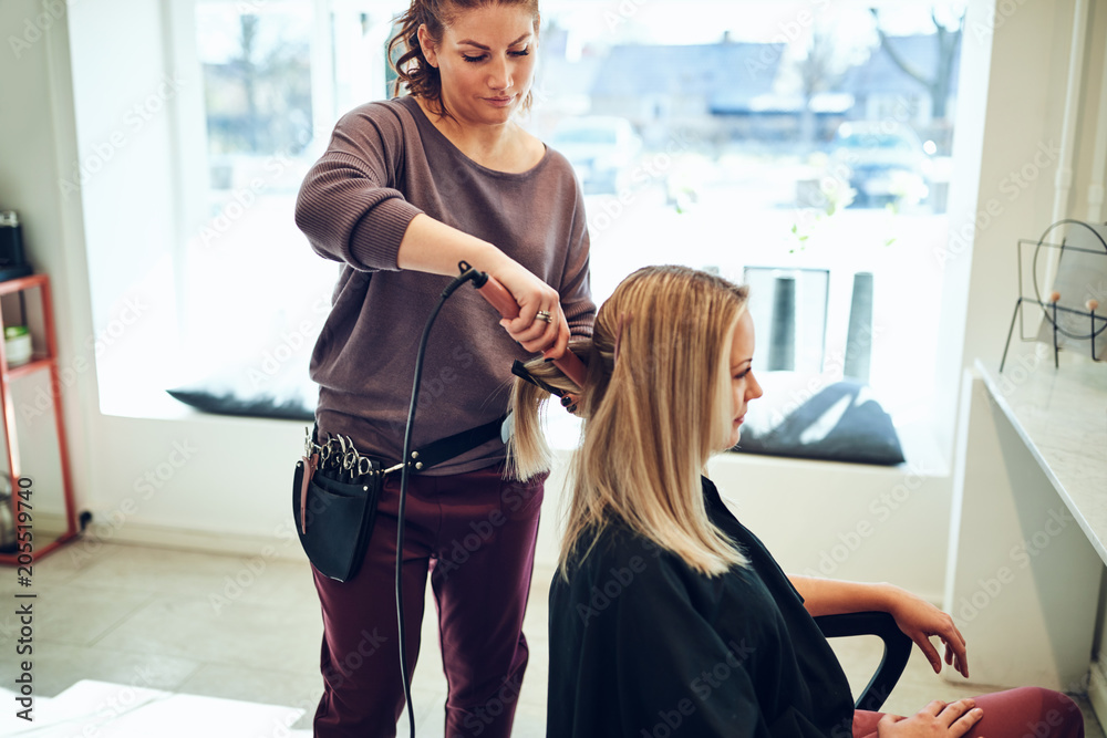 Hairstylist straightening a womans hair in her salon