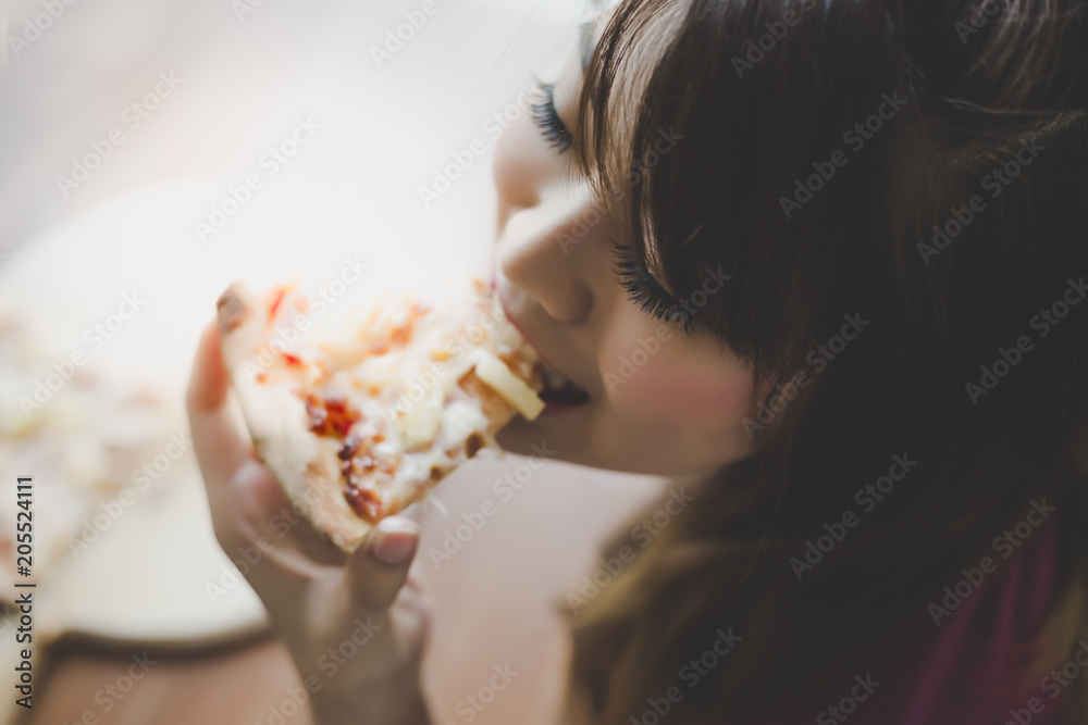 A beautiful woman is holding a piece of pizza and eating it. Pretty asian girl feels happy and enjoy