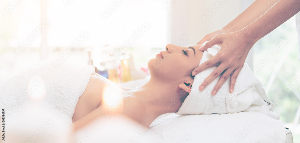 Relaxed woman gets facial and head massage in spa.