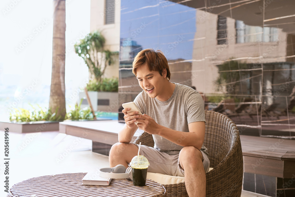 夏日阳光明媚，开朗迷人的微笑亚洲男人使用智能手机