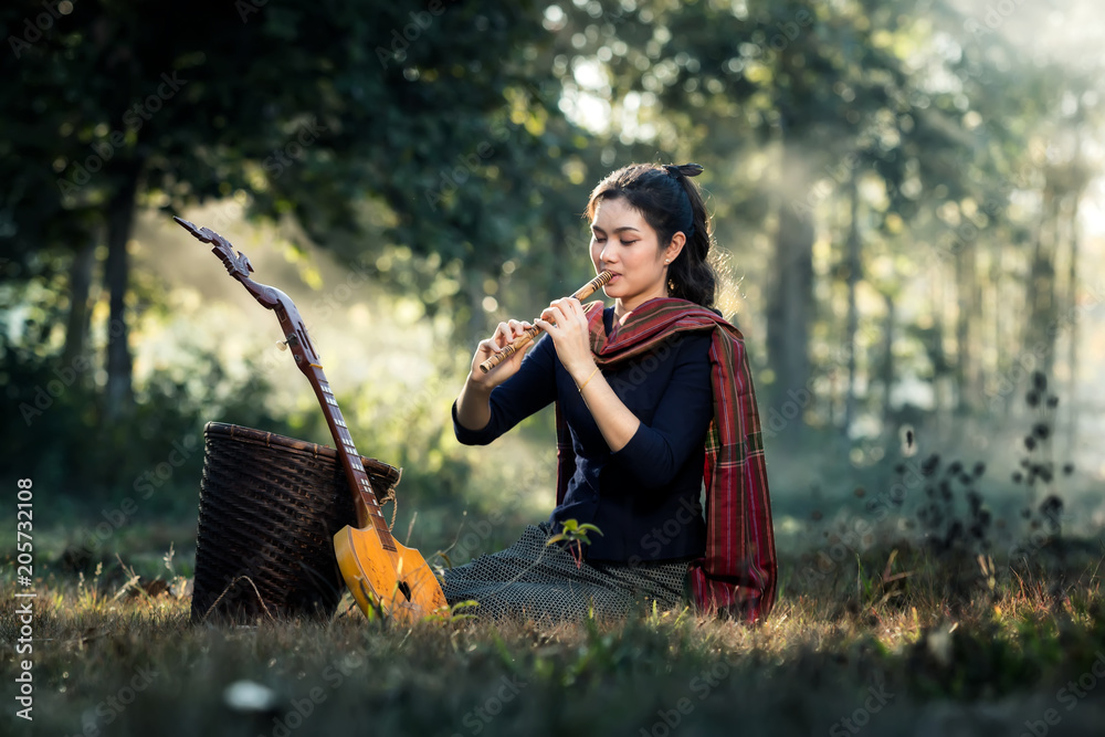 Asia women are playing on the flutes, sitting in a forest at countryside.