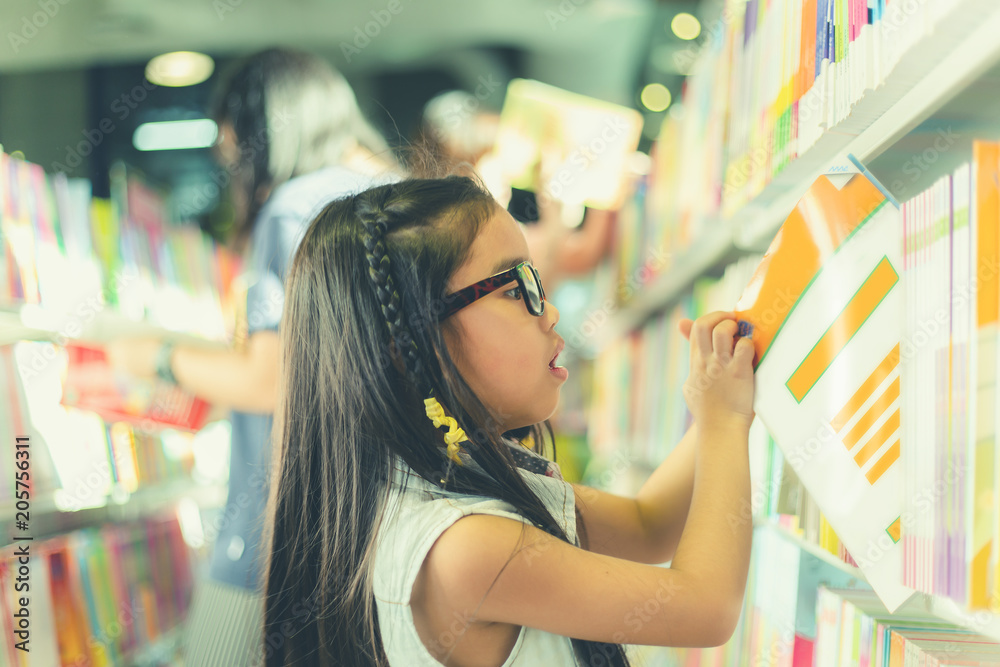 Little Asian child  picking books from the bookshelf