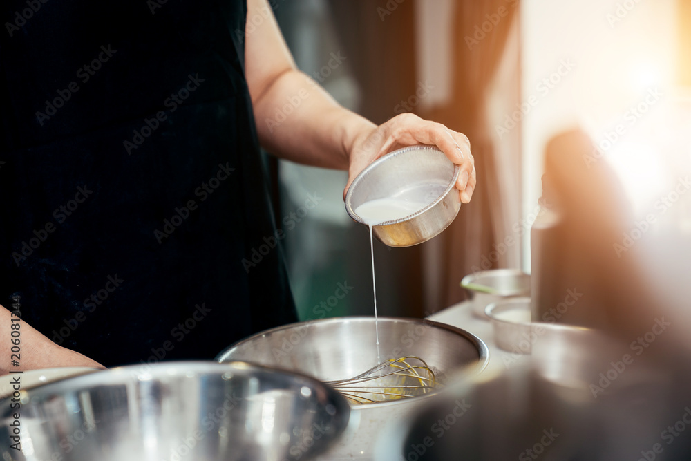 亚洲妇女在厨房里把牛奶倒进不锈钢碗里，牛奶是制作蛋糕的原料