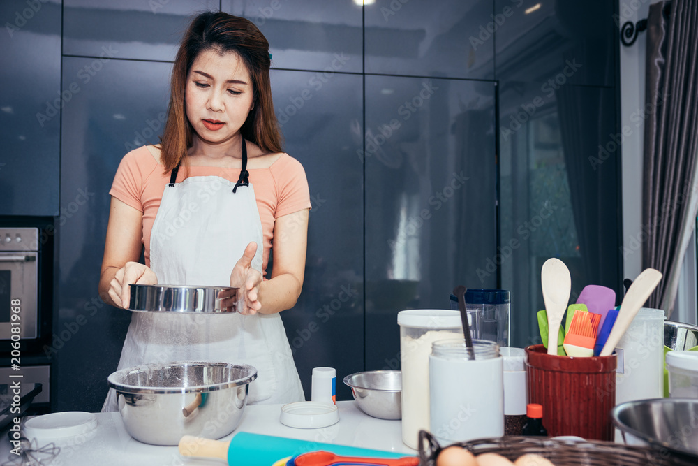 一名亚洲妇女正在碗里筛面粉。女孩正在厨房里筛面粉做面包