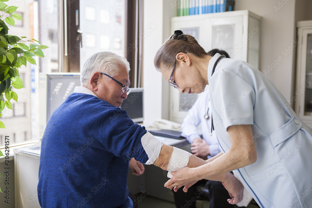 看護師が、医師の指示のもと、患者の老人の腕に包帯を巻いている。