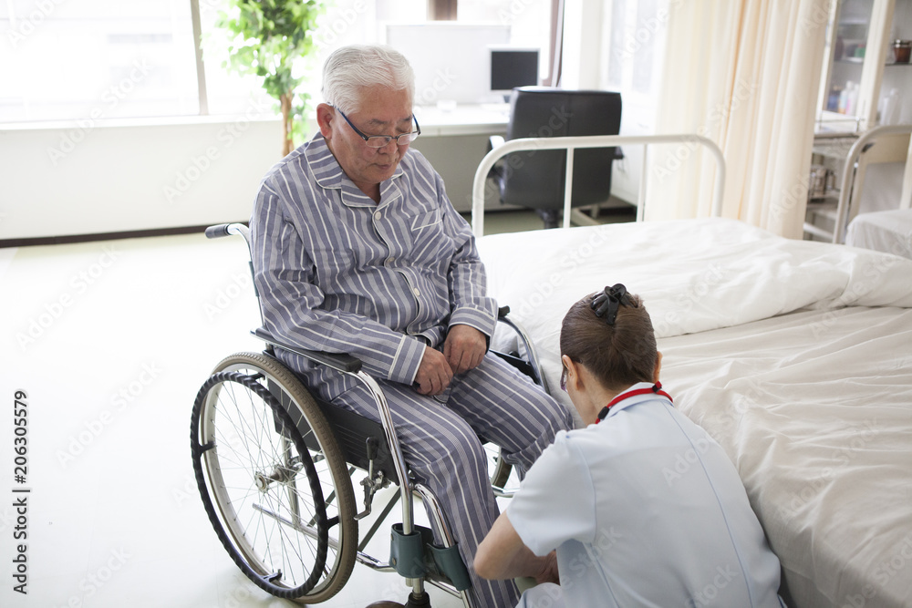 介護士が、リハビリ中の老人を車椅子に座らせている。