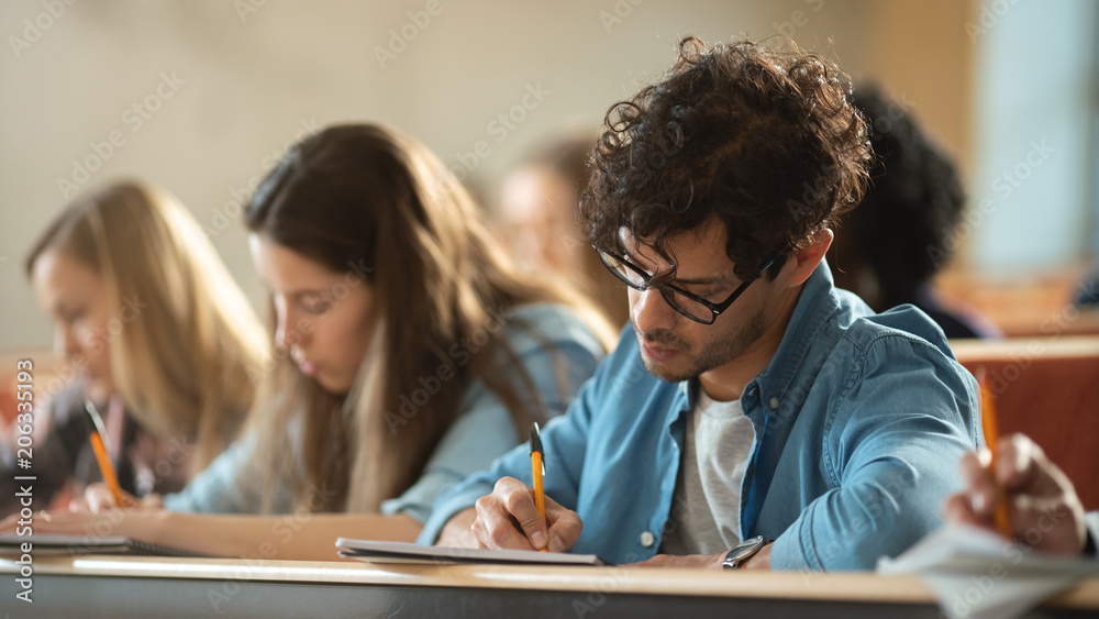 教室里一排多民族学生参加考试/考试的镜头。专注于拿笔和