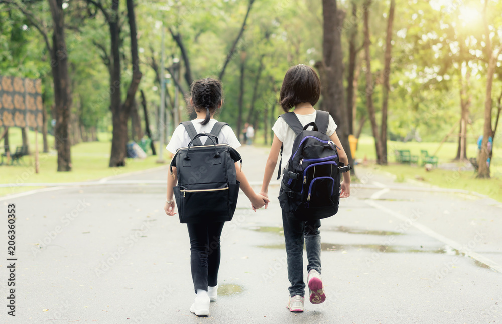 两个小学生手牵手。两个女孩背着书包。温暖的一天