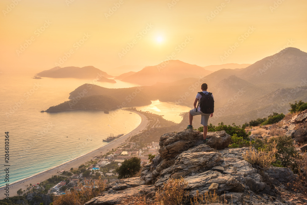 背着背包，站在岩石顶部，眺望海岸和山脉的年轻运动型男子