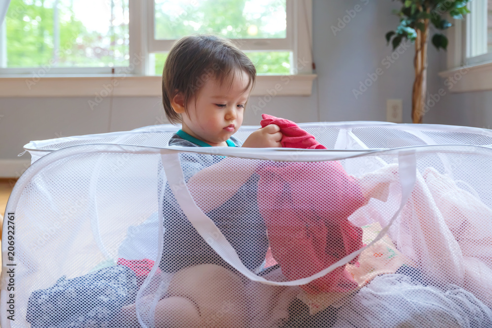 快乐的蹒跚学步的男孩在装满衣服的洗衣篮中玩耍