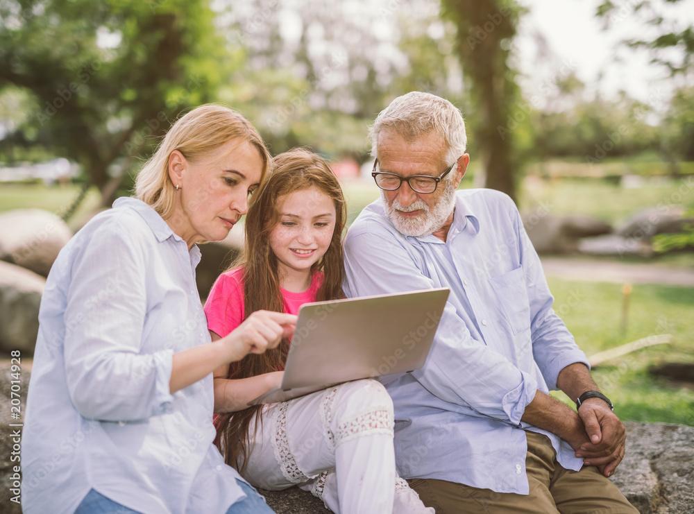 Grandfather And Grandchildren family using laptop while resting in park