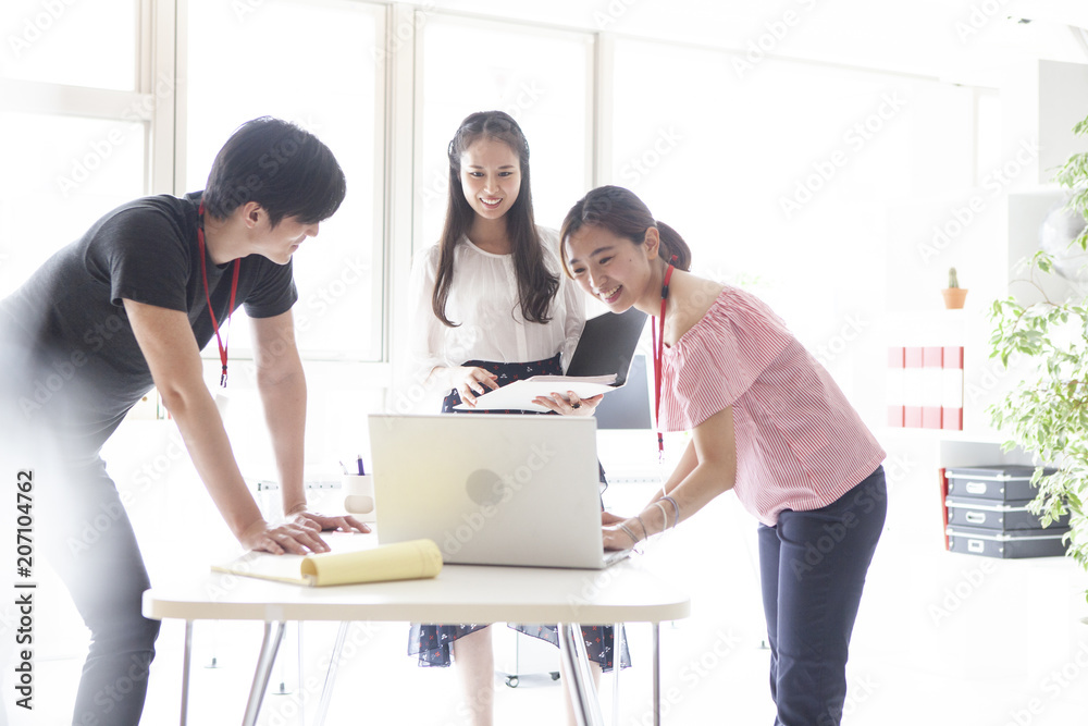 オフィスでＰＣを見ながら楽しそうに話し合う三人の男女