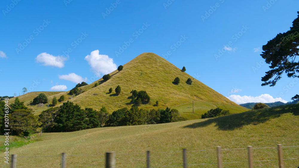 风景优美的乡村公路附近，一座陡峭的长满草的小山耸立在阳光明媚的天空中