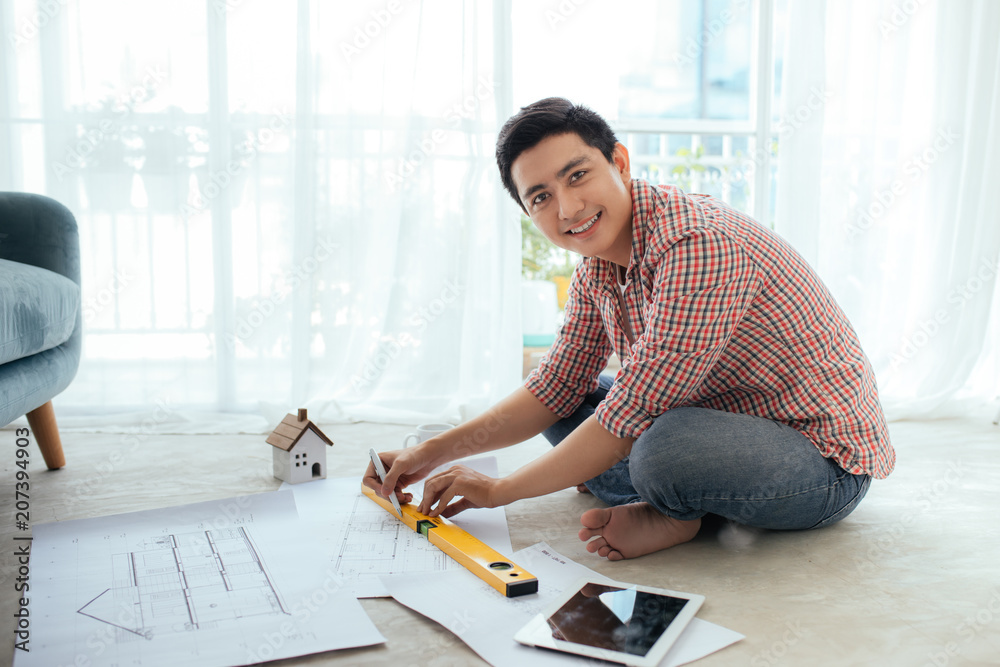 年轻英俊的亚洲男建筑师在家里的地板上工作。