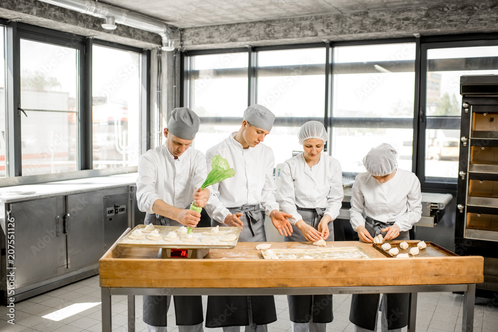 Group of young workers in uniform filling buns for baking on the wooden table standing together at t