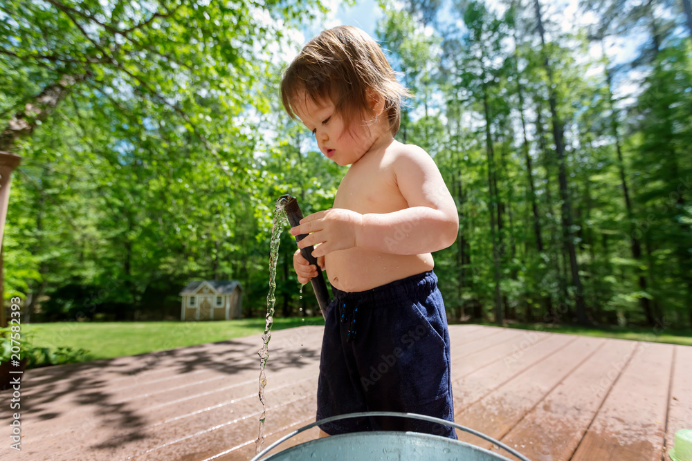 Young toddler boy playing with water from a garden hose outside