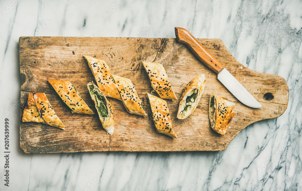 Flat-lay of freshly baked Turkish borek roll slices with spinach, feta cheese and black cumin seeds 