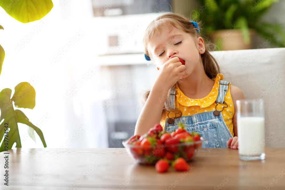 happy baby girl eating strawberries with milk