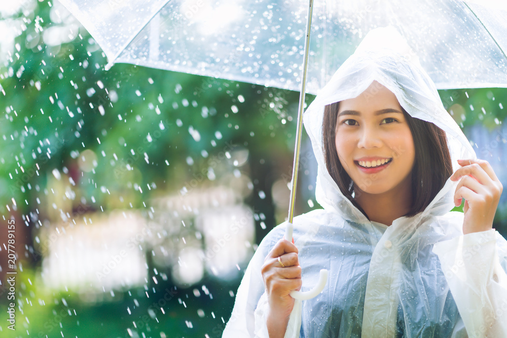 Rainy day asian woman wearing a raincoat outdoors. She is happy.