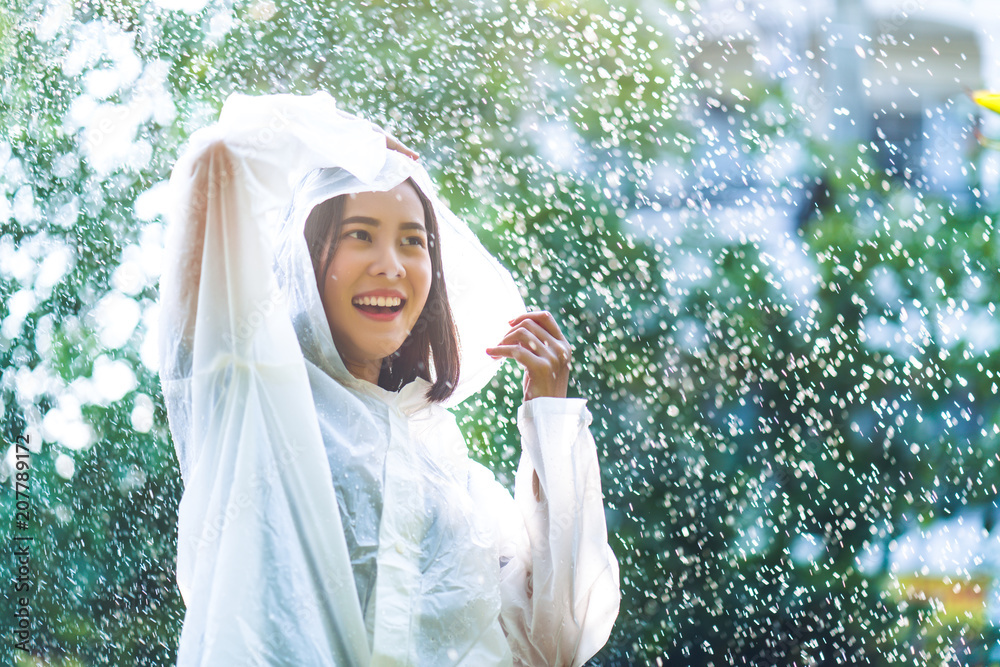 Rainy day asian woman wearing a raincoat outdoors. She is happy.