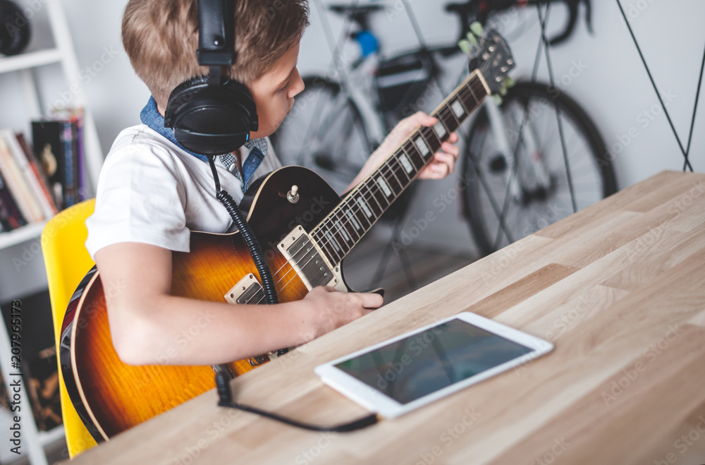 Kid boy learning to play electric guitar using tablet with headphones