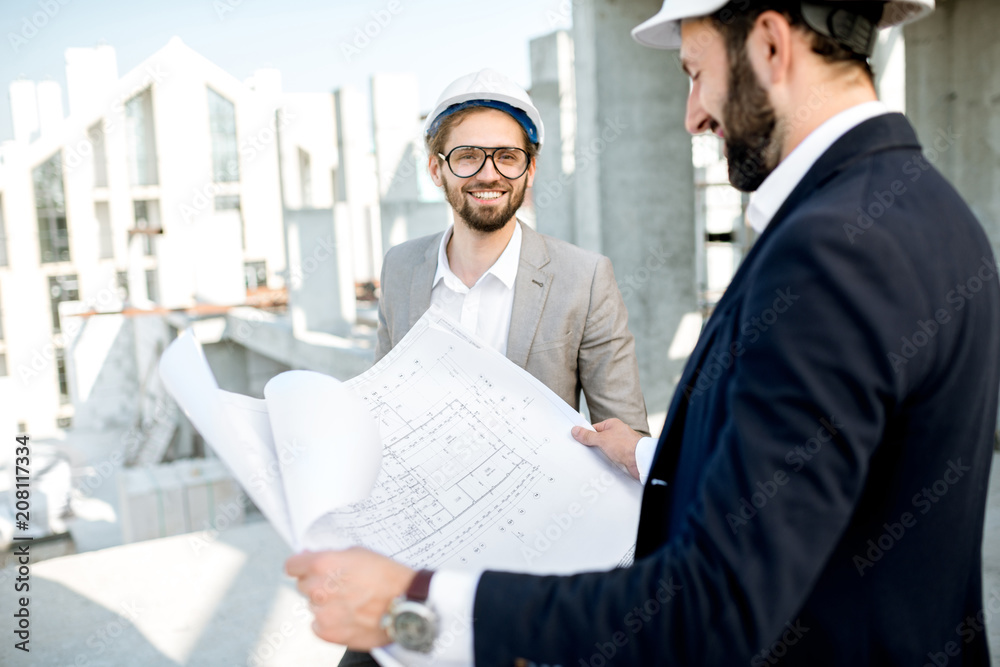 Two business men or engeneers working with house drawings on the structure during the construction p