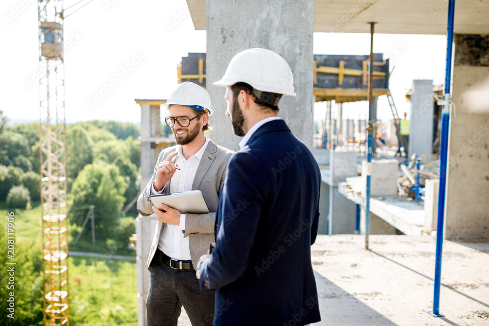 Two engineers or architects supervising the process of residential building construction standing on