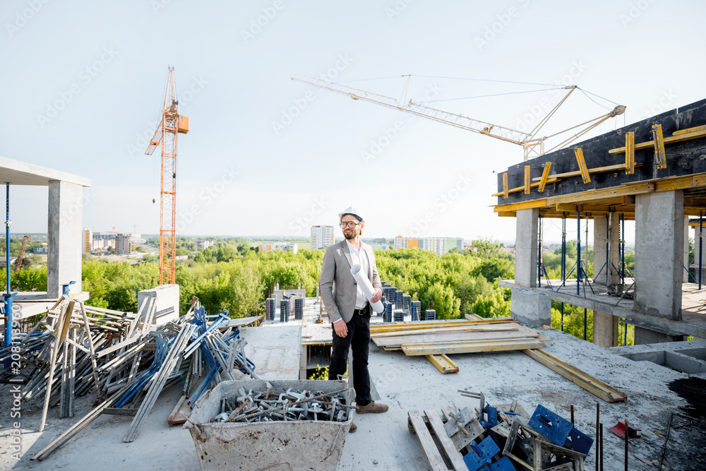 Engineer checking the construction process standing with house drawings on the structure outdoors