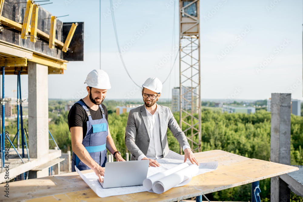 工程师和穿着制服的工人在c桌上处理建筑图纸和笔记本电脑