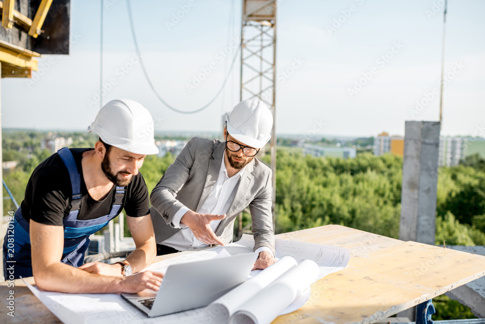 工程师和穿着制服的工人在c上的桌子旁处理建筑图纸和笔记本电脑