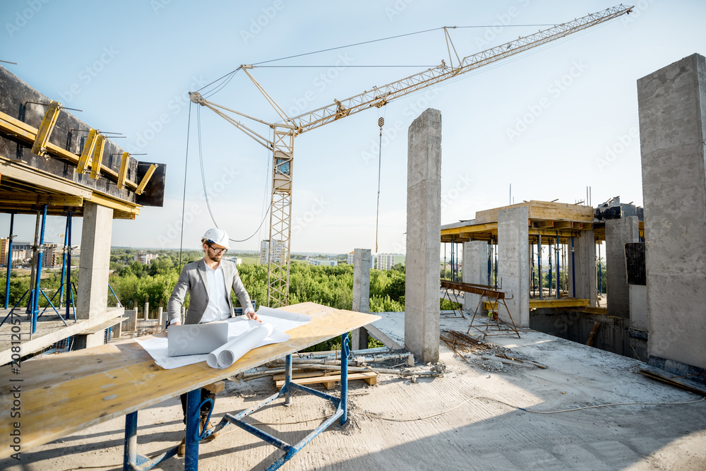 Handsome engineer working with architectural drawings at the table on the construction site outdoors