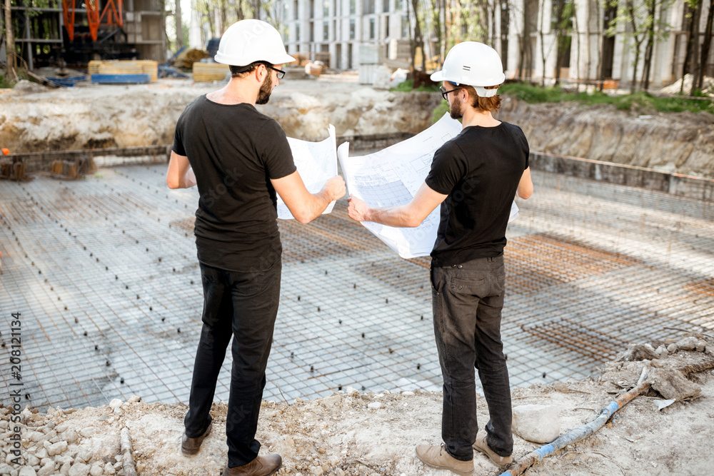 两名建筑工人站在室外的施工现场处理建筑图纸