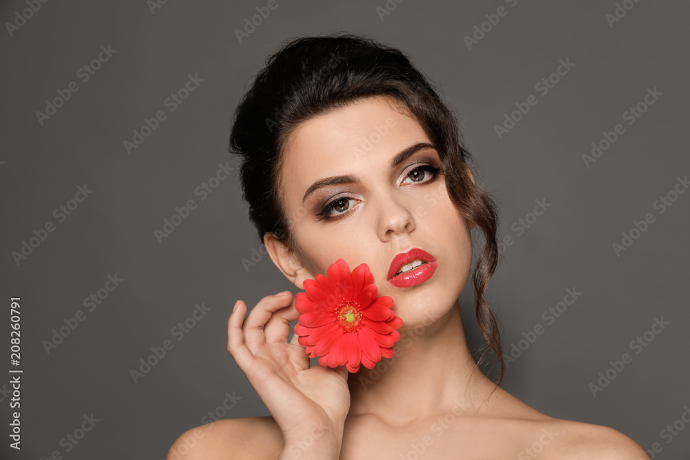 Portrait of young woman with beautiful professional makeup and flower on grey background