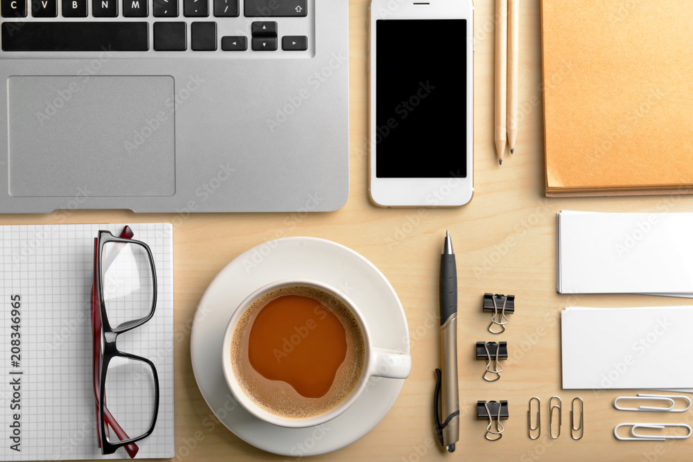 Workplace composition with laptop, cup of coffee, smartphone and stationery on table