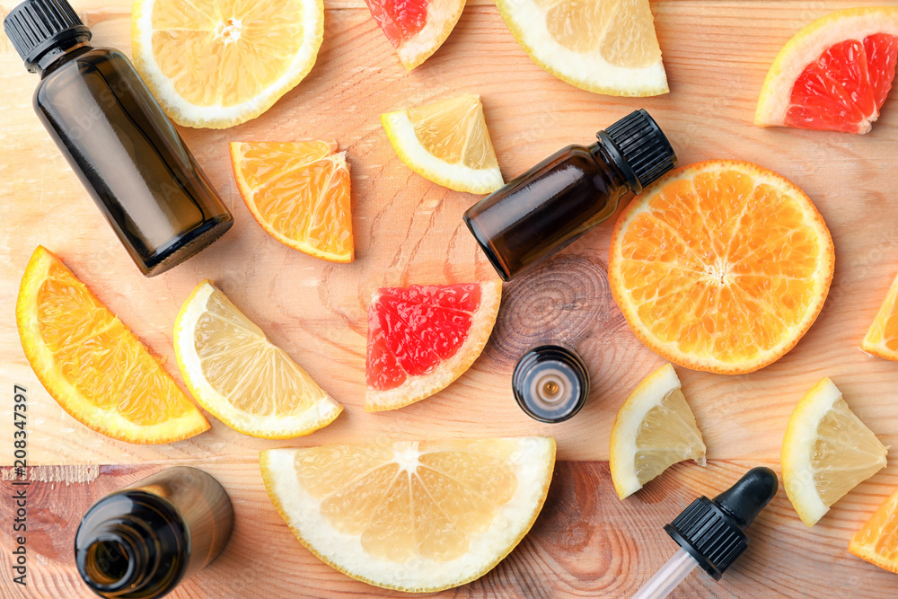 Bottles of essential oil and citrus slices on wooden table