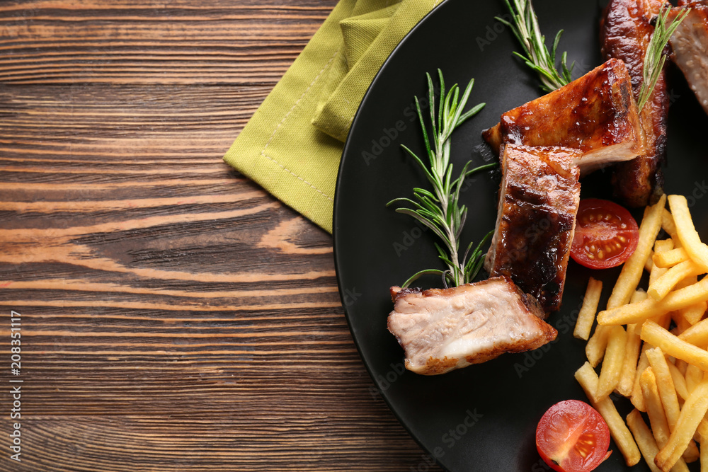 Plate with delicious grilled ribs and french fries on table