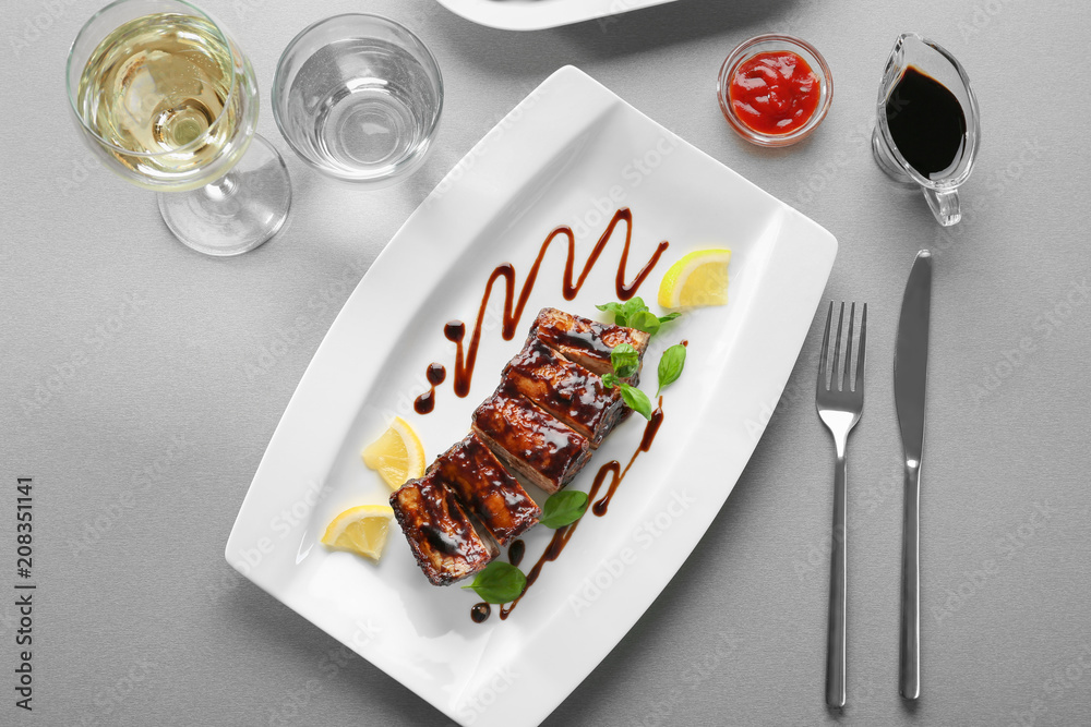 Plate with delicious grilled ribs and sauce on table