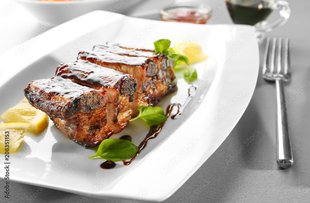 Plate with delicious grilled ribs and sauce on table