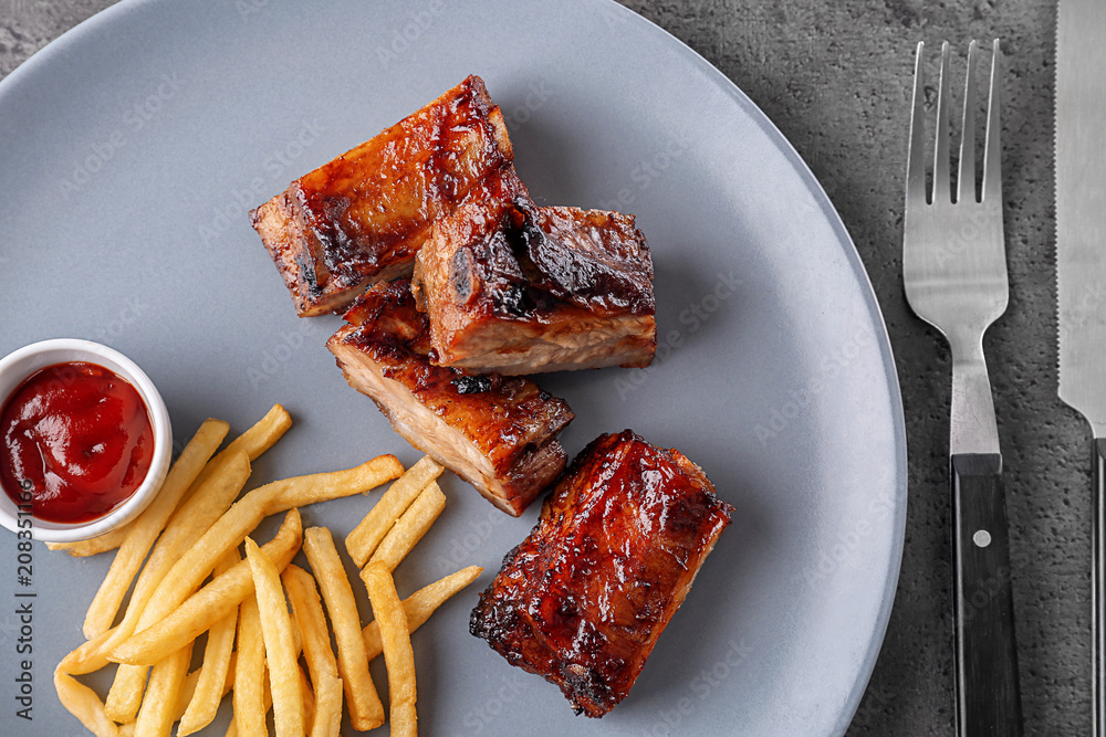 Plate with delicious grilled ribs and french fries on table