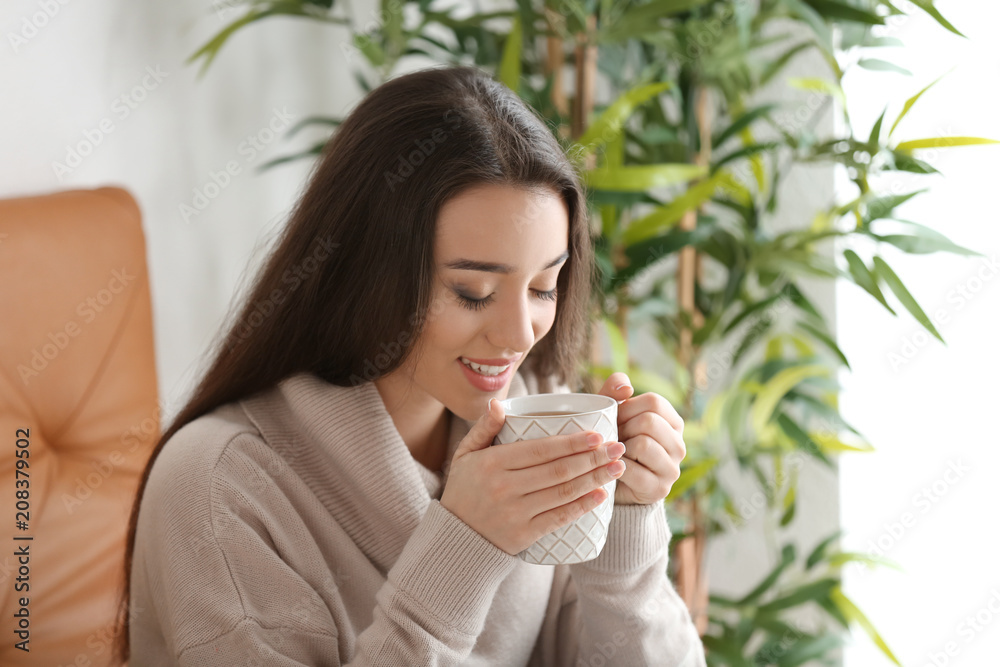 Beautiful young woman with cup of hot tea at home