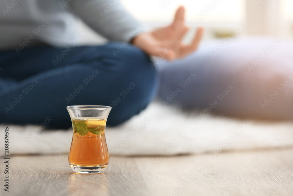 Cup of hot tea and woman meditating on floor at home