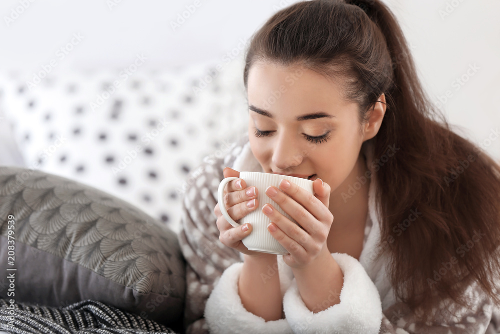 Beautiful young woman with cup of hot tea at home