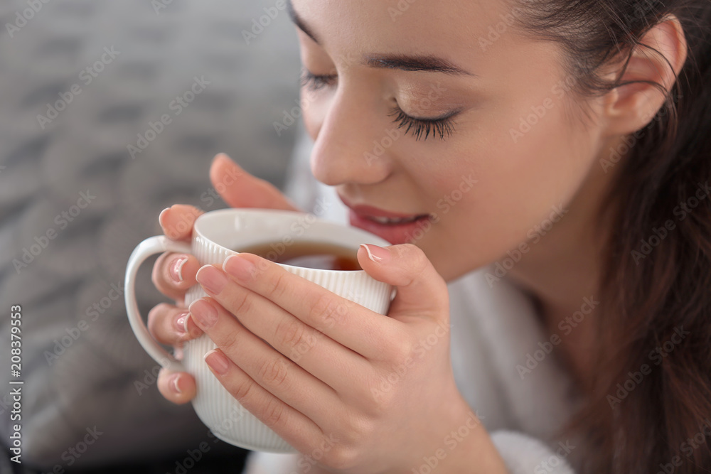 漂亮的年轻女人在家里喝杯热茶，特写